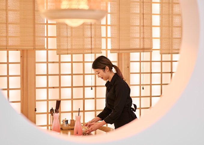 Eine Frau in einem schwarzen Shirt steht an einem Tisch eines asiatischen Restaurants in einem Einkaufszentrum